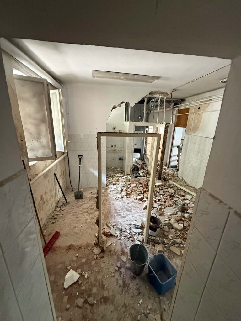 Prace wyburzeniowe w trakcie trwania. Na pierwszym planie wyburzona ściana i pozostałą do demontażu ościeżnicę. W tle ściana w trakcie wyburzania. Prace dla firmy z branży nieruchomości w Warszawie