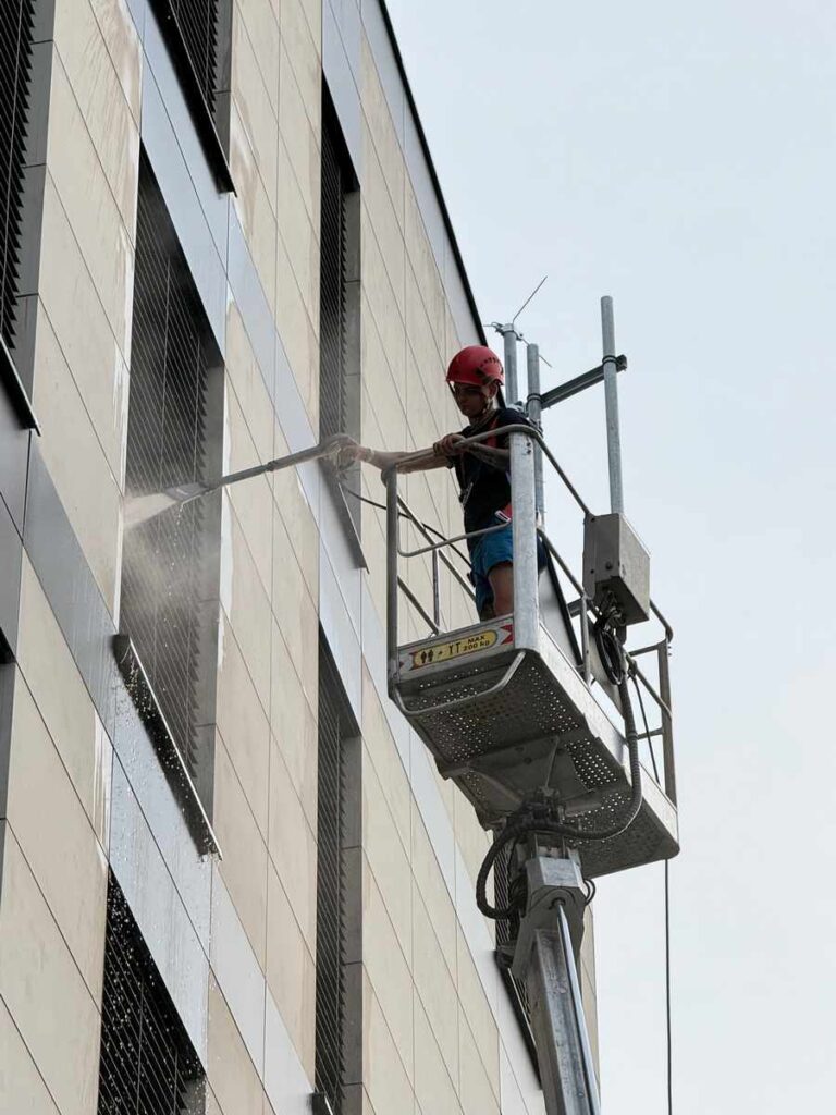 Pracownik Solid Work na podnośniku koszowym myjący elewację pod ciśnieniem